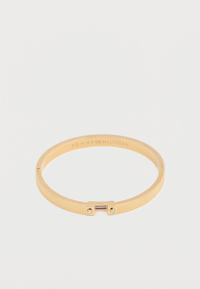 Χρυσό βραχιόλι Tommy Hilfiger με ραβδωτή υφή, μικρά κρύσταλλα στο κούμπωμα και χαραγμένο το όνομα της μάρκας στο εσωτερικό της ταινίας.