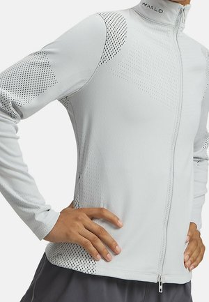 Person iført lys grå langærmet lynlåstrøje med teksturerede ventilationspaneler og HALO-logo på kraven, hænderne hvilende på hofterne.