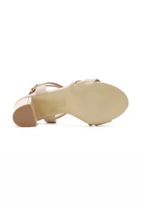 Nude high-heeled sandal with a smooth, glossy finish, featuring thin straps and a textured rubber sole. Block heel for stability.