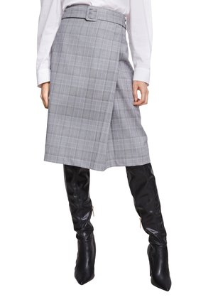 Jupe en plaid grise avec une ceinture, présentant une coupe droite et une longueur au genou. Associée à des bottes noires montantes.