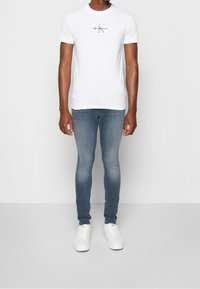 Vit kortärmad t-shirt med en svart Calvin Klein Jeans-logotyp, i kombination med blåa blekta skinny jeans och vita sneakers.