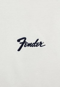 Valkoinen puuvillapaita, jossa on etuosassa keskellä suurikokoinen musta kirjailtu "Fender" -logo käsinkirjoitetussa fontissa.