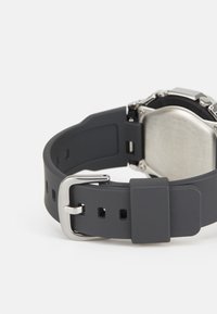 Bracelet de montre en silicone gris avec boucle en métal argenté, présentant plusieurs trous pour un ajustement et une finition texturée sur le bracelet.