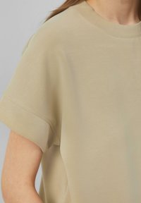Beige katoenen t-shirt met een ronde halslijn, korte mouwen en een gladde, lichtjes gestructureerde oppervlakte. Casual pasvorm met opgerolde mouwranden.