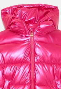 Chaqueta acolchada rosa con una textura brillante y acolchada, que presenta un alto cuello y una cremallera dorada en el frente. Material ligeramente reflectante.