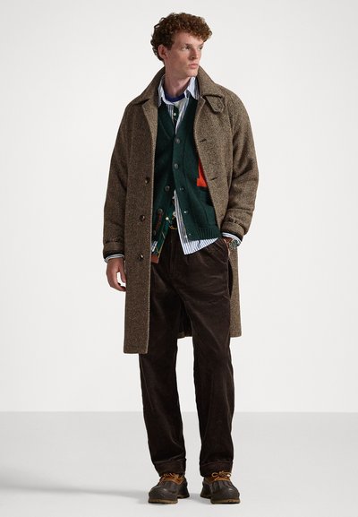 Barna halszálkás kabát, mintás zöld kardigán, csíkos ing, barna kordbársony nadrág és sötét cipők narancssárga fűzővel.