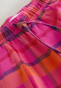 Prim-plan al pantalonilor scurți în carouri roz și portocaliu, cu talie elastică și detaliu cu șnur legat.