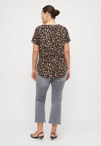 Majica s kratkim rukavima u leopard uzorku s zaobljenim rubom, uparen sa sivim skraćenim trapericama i crnim slingback cipelama, prikazuje ležeran izgled.
