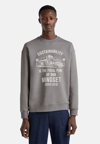 Sweatshirt gris à col rond fabriqué en tissu mélangé de coton, avec un texte graphique blanc sur le thème de la durabilité à l'avant. Le texte inclut "Soyez vert."