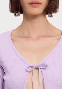 Lilac ribbed top with a deep V-neck and a bow tie detail at the center, featuring a textured fabric and fitted design.