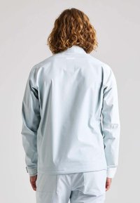 Helle blaue, wasserdichte Jacke aus glattem Material, mit langen Ärmeln und hohem Kragen. Auf der Rückseite befindet sich ein Logo und die Ärmelabschlüsse sind einstellbar.
