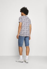 Camiseta gris de manga corta con estampado de palmeras, combinada con pantalones cortos de mezclilla azul, calcetines blancos y zapatillas deportivas gris claro.
