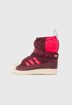 Bota deportiva de caña alta en burdeos y rosa con cierre de correa, rayas de Adidas en el lateral y suela de goma crema.