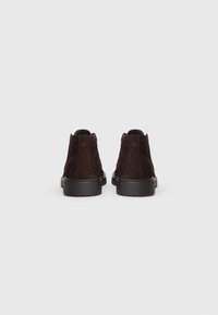 Brown suede ankle boots with a smooth finish, low heel, and textured detailing at the back. Black rubber sole for grip.