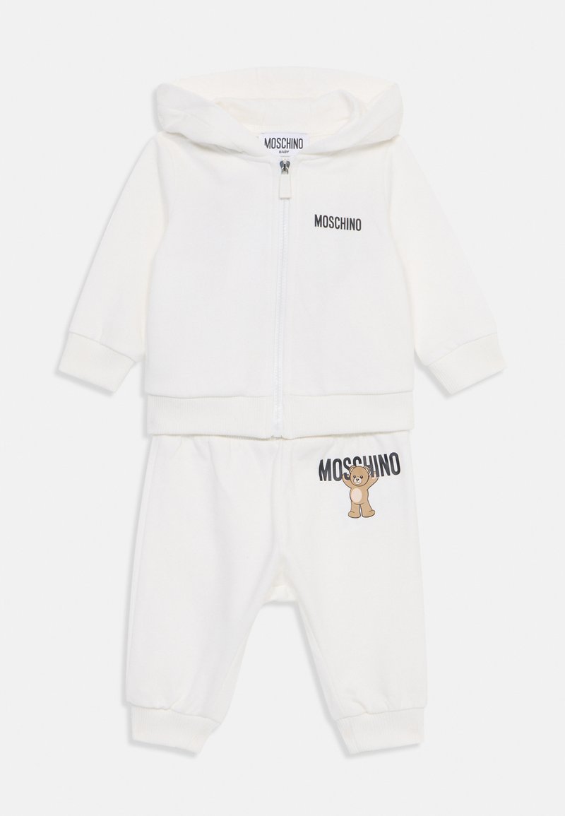 Completo per bambino bianco composto da una felpa con zip con logo "MOSCHINO" e pantaloni abbinati con un grafico di un orsetto, realizzato in morbido tessuto.
