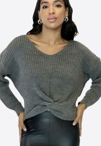 Pull gris en maille avec un col en V, coupe ample et design torsadé sur le devant. Caractérisé par des manches larges et un motif texturé. Porté avec un pantalon taille haute.