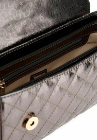 Sac à main en métal matelassé avec un motif en diamant, doté d'une fermeture à pression en métal doré et d'une poche zippée intérieure en doublure beige.