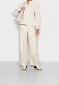 Vaaleanbeige nappipaita, jossa on liehukkeet hihansuissa, yhdistettynä kermaisiin leveälahkeisiin nahkahousuihin ja vaaleanvalkoisiin korollisiin saappaisiin. Pehmeä tekstuuri koko asussa.