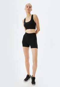 Crop top et shorts de sport noirs, réalisés en matériau lisse et extensible. Présentent un design épuré avec des coutures minimales et une silhouette ajustée.