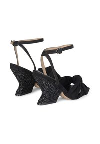 Sandali con tacco alto in suede nero, caratterizzati da un distintivo nodo anteriore e una zeppa texturizzata decorata con perline nere e motivi geometrici.