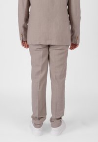 Completo in lino grigio chiaro con vestibilità su misura, caratterizzato da una giacca doppiopetto e pantaloni coordinati. Completato con sneaker bianche.