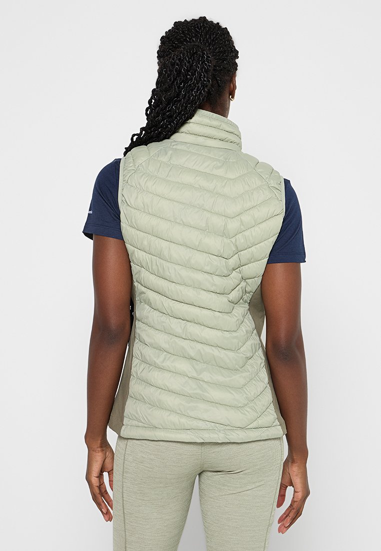 Gilet trapuntato verde chiaro con colletto alto, cuciture posteriori e una finitura liscia. Indossato sopra una maglietta blu navy e abbinato a pantaloni grigi.