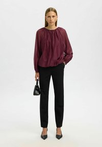 Viininpunainen, pitkähihainen paita rypytetyllä pääntiellä, yhdistetty kapeisiin mustiin housuihin ja mustiin korkeakorkoisiin kenkiin. Mukana pieni musta käsilaukku.