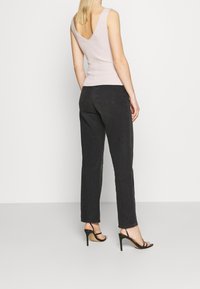 Jasnoróżowy prążkowany top na ramiączkach z głębokim dekoltem na plecach, zestawiony z czarnymi jeansami o prostym kroju i czarnymi sandałami na obcasie z paskami.