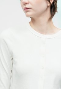 Lähivõte inimesest, kes kannab valget nööbiga särk, vaatab kõrvale, lühikeste pruunide juustega ja neutraalse ilmega.