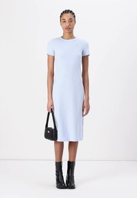 Light blue, short-sleeved dress made from smooth fabric, fitted silhouette, knee-length. Paired with a black handbag and ankle boots.