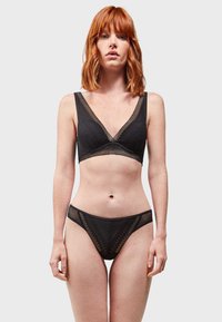 Completo di lingerie nera composto da un bralette con scollo a V in rete testurizzata e motivi geometrici, abbinato a slip a vita bassa coordinati.
