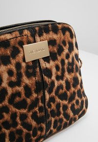 Torebka w cętkowany wzór z miękkiego materiału, złotymi detalami i metalową tabliczką z napisem "RIVER ISLAND". Zamykanie na zamek u góry.