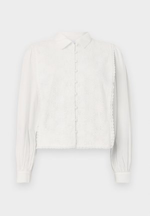 Hvit bluse med krage, knapplukking og blomsterlacemønster på forsiden. Lange ermer med samlet mansjett og bølgende kanter.