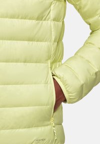 Hellgelbe Pufferjacke aus Pertex-Gewebe mit gestepptem Design, mit seitlichen Reißverschlusstaschen und elastischen Bündchen für Komfort und Isolierung.