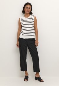 Haut sans manches blanc avec des rayures noires, associé à un pantalon noir et des sandales à talons blocs noires, avec une coupe décontractée et une texture lisse.