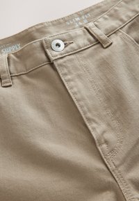 Slim fit khaki broek met een gladde textuur, voorzien van een metalen knoop en riemlussen. Gedetailleerd stiksel langs de voorkant van de zak.
