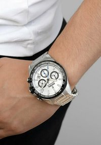 Montre en acier inoxydable argenté avec un cadran blanc, trois sous-cadrans noirs, une lunette noire et un affichage de la date. Portée au poignet, avec une finition brossée.