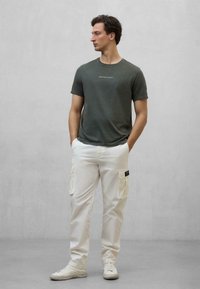 Mørkegrøn crew-neck t-shirt med en hvid tekstdetalje, parret med løs siddende hvide cargo-bukser med sidelommer og sorte accenter.