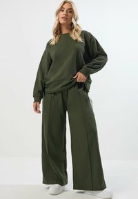 Olivgrön långärmad sweatshirt och set med vida byxor. Mjukt tyg med avspänt snitt. Matchas med vita sneakers.