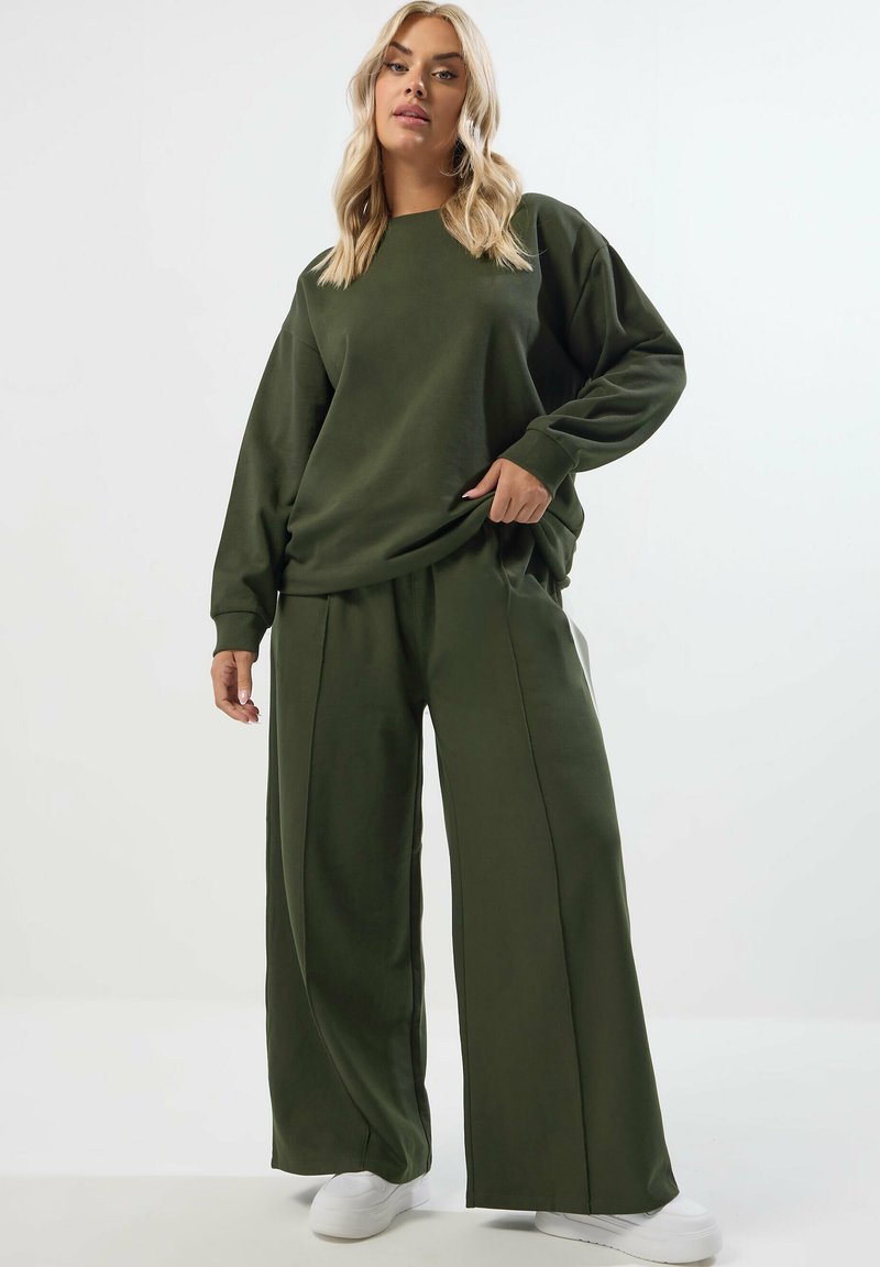 Olivgrön långärmad sweatshirt och set med vida byxor. Mjukt tyg med avspänt snitt. Matchas med vita sneakers.