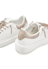 White sneakers with a textured beige suede heel, flat white rubber sole, and metallic gold laces. Round toe and low-top design.