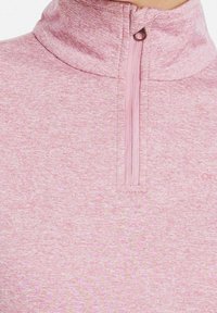 Ljust rosa, texturerad tröja med dragkedja i halsen, i ett mjukt tyg utan synliga mönster. Förstärkt sömnad nära dragkedjan.