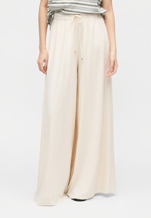 Pantalon beige à jambes larges avec taille à cordon porté avec une chemise rayée rentrée, montrant seulement le bas du torse et les jambes.