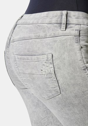 Graue Denim-Jeans verfügen über ein enges Design mit einer Gesäßtasche, die mit dekorativen Nieten verziert ist, und einer dezenten, ausgewaschenen Textur.
