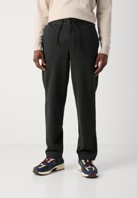 Pantalons de survêtement gris foncé avec une taille à cordon, poches latérales et coupe décontractée, associés à des chaussures de sport multicolores.
