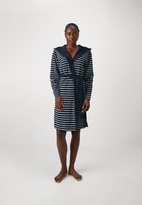 Accappatoio con cappuccio caratterizzato da strisce orizzontali blu navy e bianche, maniche lunghe, una cintura annodata e una consistenza morbida. La lunghezza arriva sopra le ginocchia.