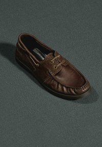 Hnědá kožená nazouvací bota s kulatou špičkou, dekorativním prošíváním a dvěma zlatavými průchodkami. Hladká textura a měkká, pružná podrážka.