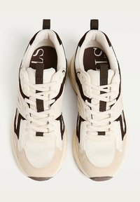 Baskets beiges et marron avec une tige en maille, des panneaux texturés, un bout rond et un design à lacets. Comprend une languette au niveau du talon.
