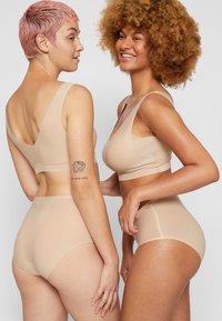 Two models wear matching nude bralettes and high-waisted underwear showcasing seamless design, smooth texture, and a minimalist look.