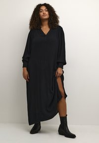 Black maxi dress with loose fit, long sleeves, V-neck, button detail, and high side slit. Paired with black ankle boots. Soft texture.